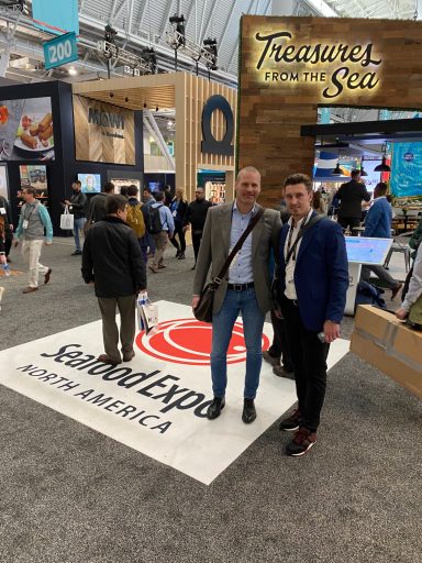 Zwei Männer posieren vor einem Stand bei einer Messe mit dem Logo "Seafood Expo".