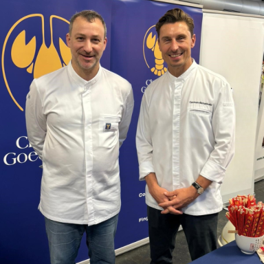 Zwei Männer in weißen Hemden stehen lächelnd vor dem Christian Goedeken Messe-Stand mit Hummerlogo.