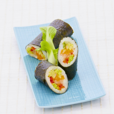 Drei bunte Sushi-Rollen auf einem blauen Teller, garniert mit Blattsalat.
