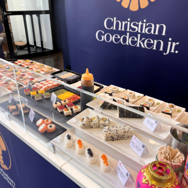 Ein Messetresen mit vielen angerichteten Tellern mit verschiedenen Sushi-Sorten und  Produktbeschilderung.