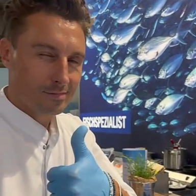 Ein Mann mit Daumen hoch in blauer Handschuh, vor einem Hintergrund von Fischen.