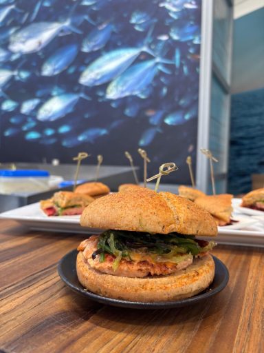 Ein Teller mit mehreren Burgern auf einem Tisch, im Hintergrund Fische und Wasser.