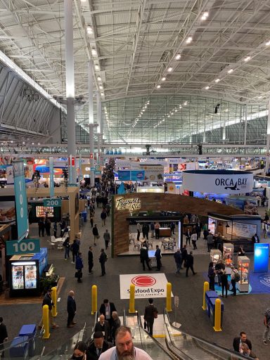 Überblick über eine große Messe mit vielen Ständen und Besuchern in einer hellen Halle.